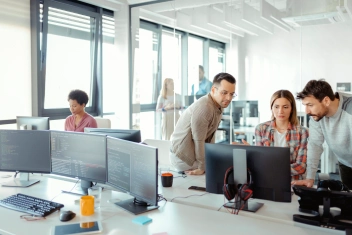 team collaborating in a modern office with multiple computer screens, illustrating open it’s software asset management solutions for optimizing software resources and ensuring efficiency.